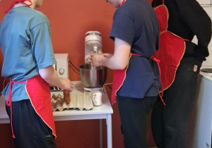 Trzech chłopców stoi obok miksera, wsypując produkty do miski.