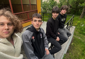 Czterech chłopców siedzących obok siebie na barierce nawiązując do znanego zdjęcia "lunch stop a Skyscraper"