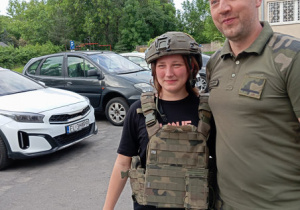 Jedna wychowanka ubrana w kamizelkę taktyczną i hełm, stoi obok żołnierza