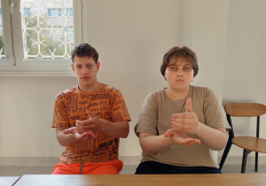 Wychowankowie siedzą pokazują znak migowy - kawa
