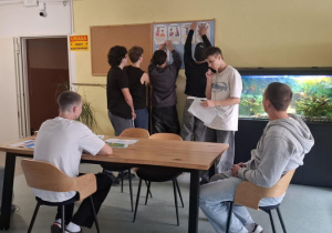 Pięcioro wychowanków przywiesza na tablicy karty tematyczne czworo wycina przy stole.