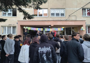 Grupa wychowanków stoi tyłem do budynku bursy w oddali widać wychowawców.