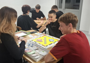 Czworo chłopców I dziewczyna grają przy stolikach w gry planszowe.