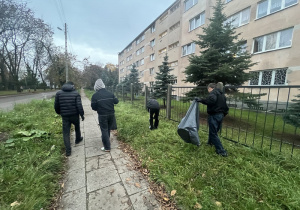 Czterech chłopców zbiera śmieci z trawnika obok bursy