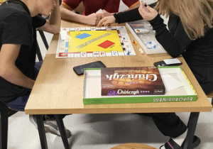 W tle dwóch wychowawców i wychowanek grają w menory, w centrum zdjęcia trzech wychowanków gra w grę planszową Eurobiznes