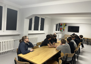 Wychowankowie siedzą przy stole i słuchają wykładu informacyjnego