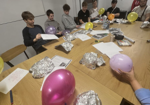Wychowankowie siedzą przy stole i wykonują prace plastyczne - autoportret z wykorzystaniem różnych materiałów (balony, folia aluminiowa, kartki, mazaki).