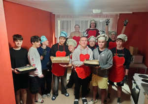 Jedenastu chłopców stoi ubranych w fartuchy i czapki trzymając w rękach ciasto.