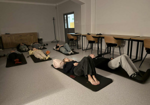 Dziewczęta leżą na matach na podłodze w sali, ubrane w wygodne ubrania i relaksują się.