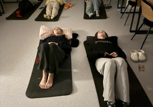 Dziewczęta leżą na matach na podłodze w sali, ubrane w wygodne ubrania i relaksują się.