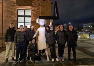 Wychowankowie wraz z wychowawcą stoją pod rzeźbą