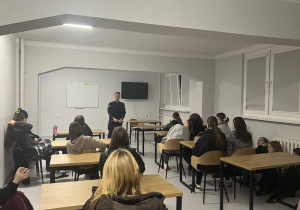 Wychowanki siedzą przy stolikach i słuchają wypowiedzi przedstawiciela Policji