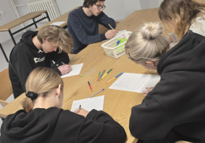 Przy stole siedzi grupa dziewcząt i chłopców, którzy rozwiązują zadania.