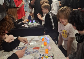 Na pierwszym planie widać chłopców siedzących przy stoliku, w oddali młodzież stoi.