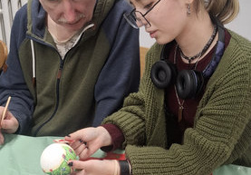 Dziewczyna pomaga oklejać styropianową bombkę kolorową serwetką