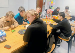 Osiem osób siedzi przy stole i gra w gry planszowe