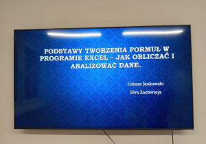 Na telewizorze jest wyświetlona prezentacja dotycząca program Excel. Na slajdzie widoczny jest tytuł zajęć