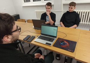 wychowankowie siedzą przy stole. Na stole leżą laptopy z włączonym programem, w którym wychowankowie wykonują zadania
