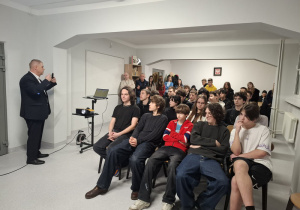 Wychowankowie siedzą na krzesłach i słuchają prelekcji.