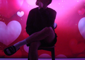 wychowanek w pozycji siedzącej pozuje do zdjęcia w tle widać walentynkowe tło, po bokach jest umieszczone światło powodujące zmianę wyglądu tła