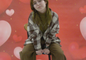 Wychowanka siedzi na krześle pozując do zdjęcia na walentynkowym tle