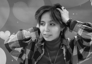 Aparat jest ustawiony w tryb czarno biały, na zdjęciu widać wychowankę z ułożonymi na głowie dłońmi, wychowanka patrzy w prawo, zdjęcie jest czarno białe.