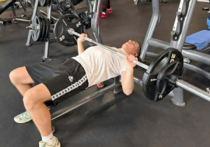 Jeden chłopiec leży na ławce poziomej i wyciska sztangę