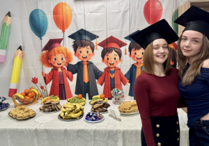 Dwie dziewczyny pozują do zdjęcia na tle przygotowanego poczęstunku